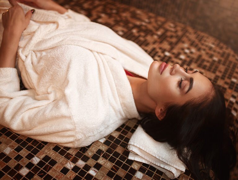 Esta chica está tumbada en el interior de un baño turco. Parece estar muy relajada. Lleva un albornoz.