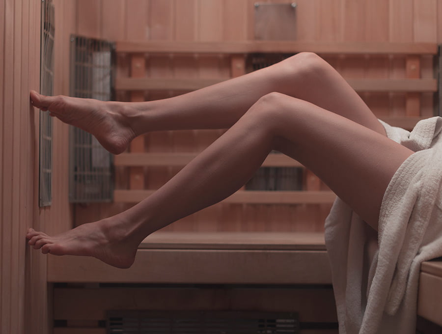 Esta chica está tocando la pared de la sauna con la punta de los pies. Está sentada en el banco.