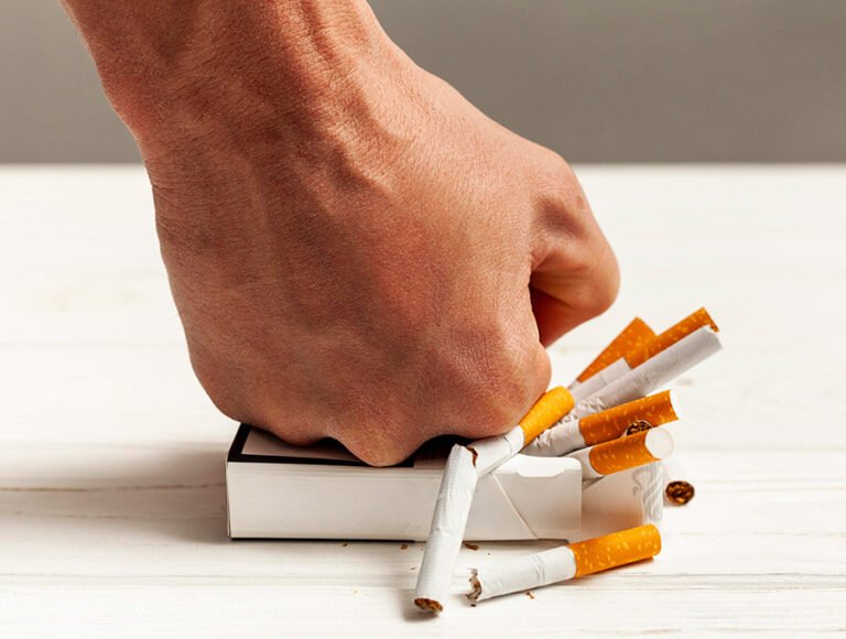 Una persona le da un puñetazo a un paquete de tabaco. Hay cigarros rotos.