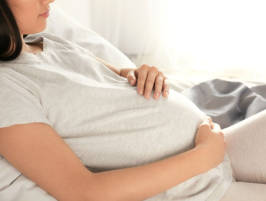 Mujer embarazada tocando su barriga en el sofá.
